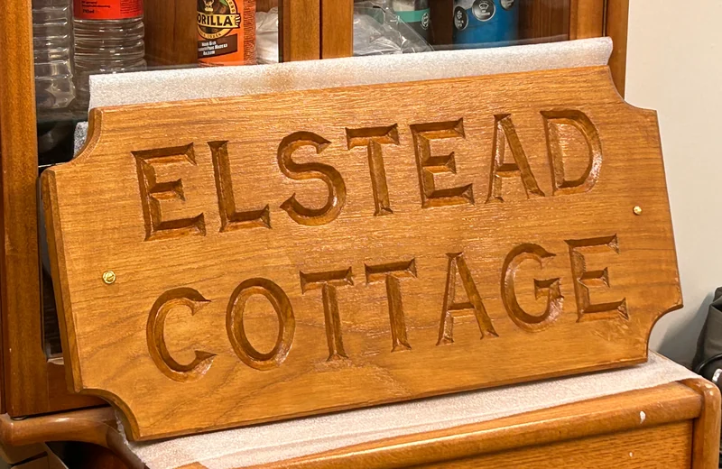 The finished Elstead Cottage wooden sign with carved lettering and shaped corners, resting in the workshop.