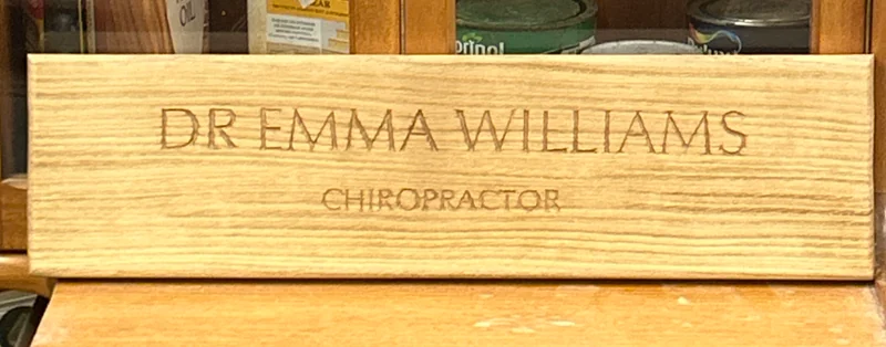 The finished wooden sign reading Dr Emma Williams, Chiropractor, photographed in the workshop.