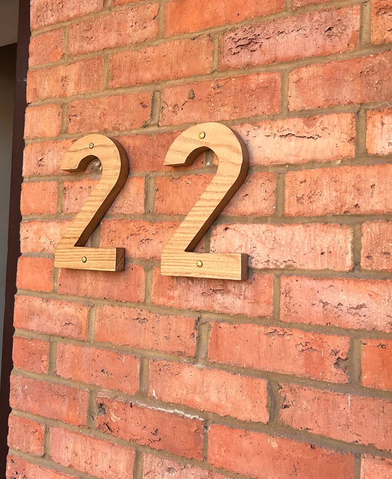 The wooden house number 22 installed on brickwork, with the grain and fixings visible.